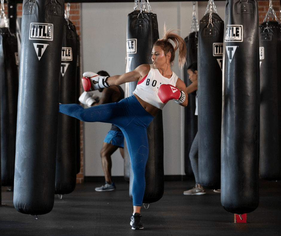 Woman kicking a heavy bag during a cardio kickboxing class at TITLE Boxing Club