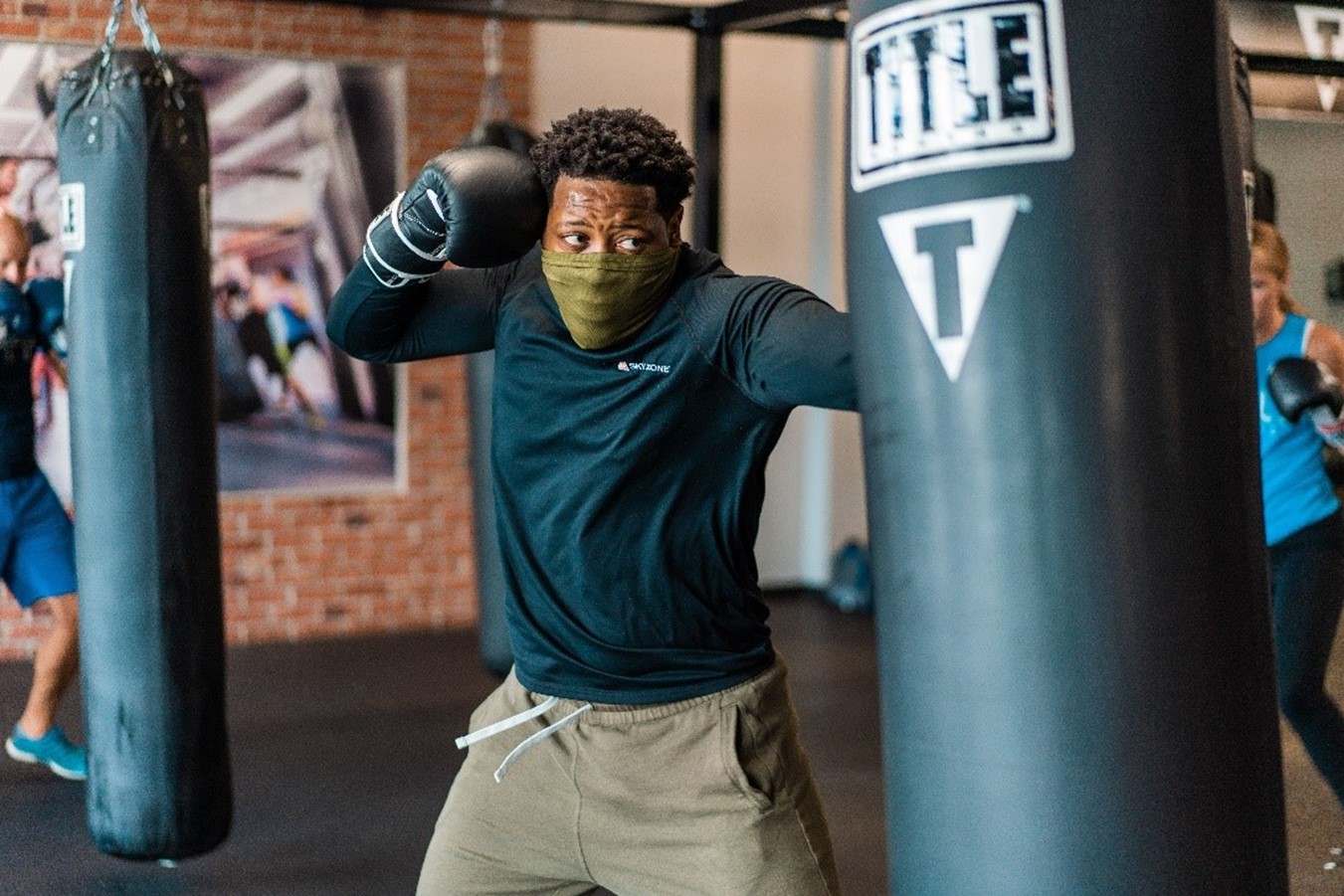 Man wearing a mask, punching a heavy bag in a TITLE Boxing Club class